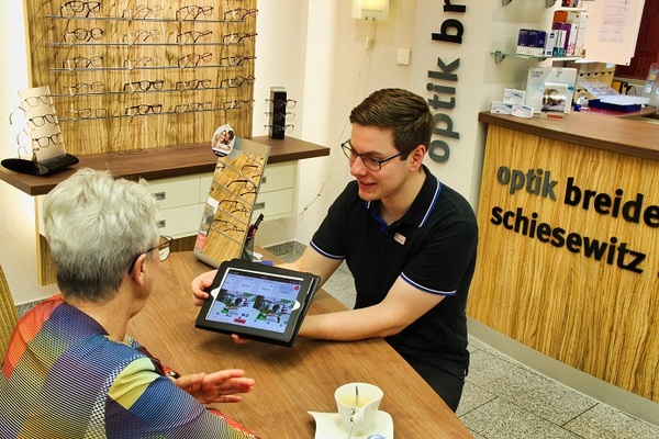 Ein Optiker berät eine Kundin mit Tablet in einem modernen Optikgeschäft.