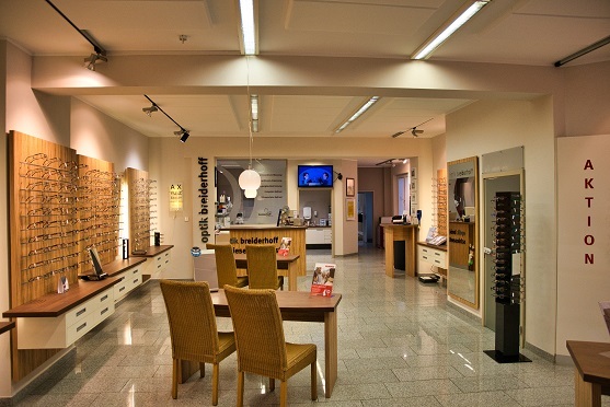 Modernes Optikgeschäft mit Brillenauswahl, Beratungstisch und heller Beleuchtung.