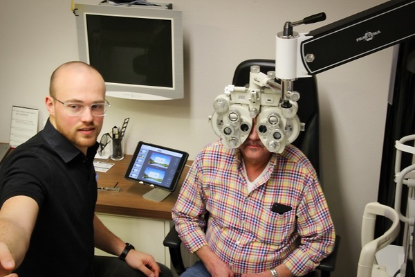Ein Optiker führt einen Sehtest mit modernem Phoropter-Gerät in einer Augenarztpraxis durch.